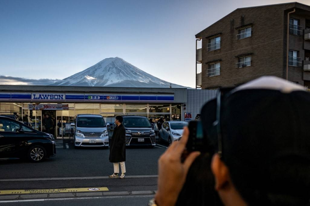 STRIKING SIGHT A man takes a picture of a tourist about to pose in front of a Lawson convenience store, with Mount Fuji in the background, in Fujikawaguchiko town, Yamanashi prefecture, central Japan on Jan. 1, 2024. AFP FILE PHOTO