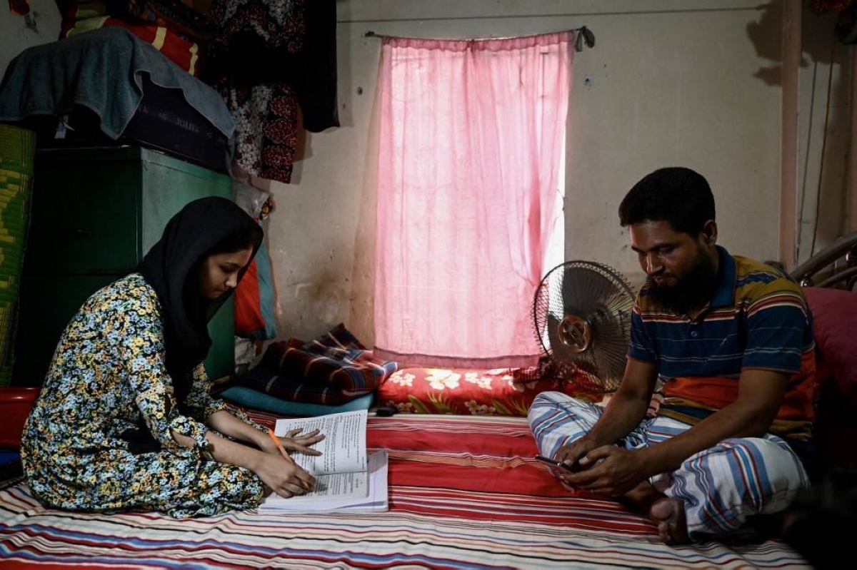 STUCK INDOORS Mohammad Yusuf (right) uses his mobile phone as he sits beside his daughter Lamia Akter, who is studying at home after in-person classes were canceled due to the heat wave, in Bangladesh’s capital Dhaka on Thursday, April 25, 2024. AFP PHOTO